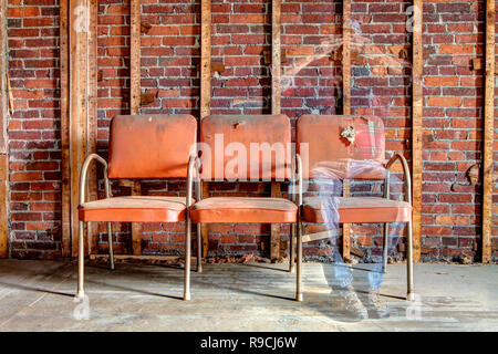 Ghostly image of a man sitting on an orange chair fading away see-through body in abandoned building. Stock Photo