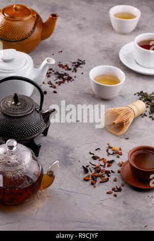 Tea card. Variety of teapots and cups on a gray background and different types of tea. Tea still life. Concept. Stock Photo