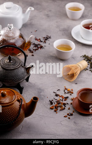 Tea card. Variety of teapots and cups on a gray background and different varieties of tea. Tea still life. Concept. Stock Photo