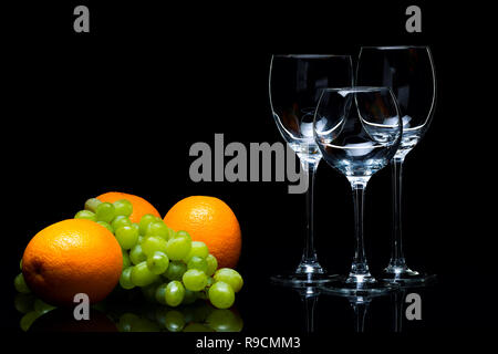 Three glasses for wine, a bunch of grapes and oranges on a black background, studio light Stock Photo
