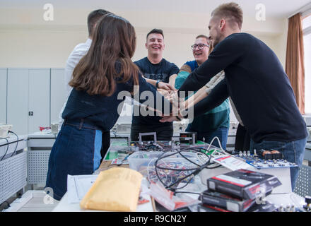 Group of young students in electronics classroom celebrating successfully finished project with holding their hands together, education and technology Stock Photo