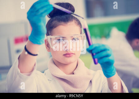 young female student with protective glasses making chemistry experiment in bright laboratory,education and medicine concept Stock Photo