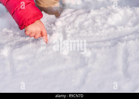 A little girl's hand writes a finger in the snow on a sunny winter day.