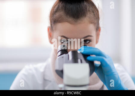 Young female student scientist looking through a microscope while doing some research in the laboratory Stock Photo