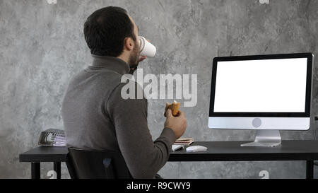 Business man in the office having breakfast, lunch and watching something on the mac, computer. White Display. Stock Photo
