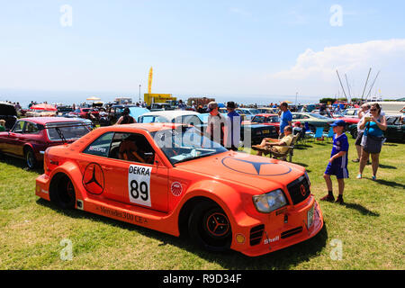 Bucket and spade classic car show on Ramsgate seafront. Orange coloured Mercedes 300CE race car, Dekra 89. Many cars and people in background. Stock Photo