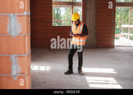 Man Working In Construction Site Smiling And Using Smartphone Stock Photo