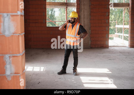 Man Working In Construction Site Smiling And Using Smartphone Stock Photo