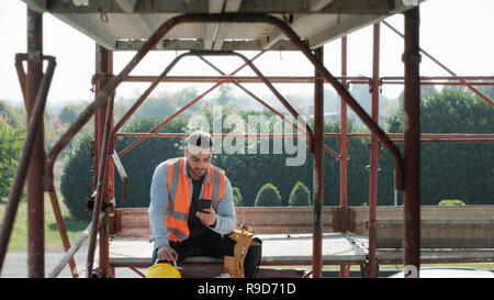 Man Working In Construction Site Smiling And Using Smartphone Stock Photo