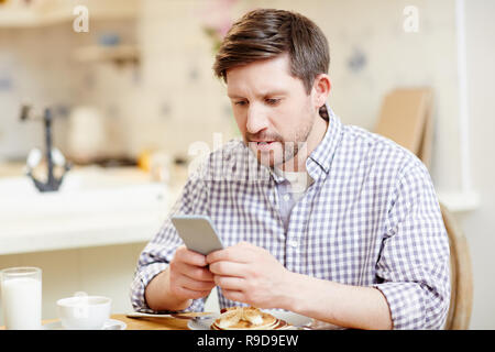 Concentrated man using smartphone at breakfast Stock Photo