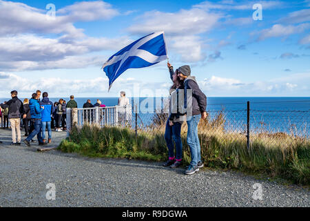 ISLE OF SKYE / SCOTLAND - OCTOBER 14 2018 : Tourists visiting the Kilt Rock waterfall by Staffin with a waving flag. Stock Photo