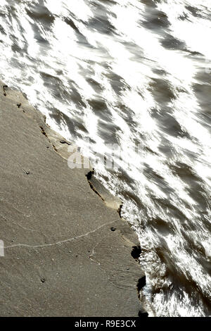 the edge of the sandy river bank is collapsing as the base is undermined by the fast flowing water Stock Photo