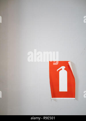 peeling off orange fire extinguisher sign sticker on white light wall Stock Photo
