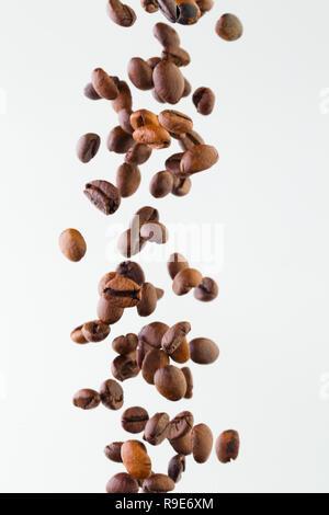 Grains of roasted coffee falling on white background, studio light Stock Photo