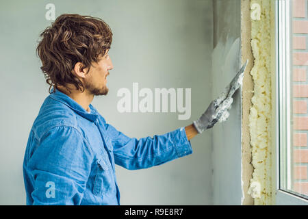 master is applying white putty on a wall and smearing by putty knife in a room of renovating house in daytime Stock Photo
