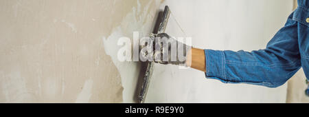 master is applying white putty on a wall and smearing by putty knife in a room of renovating house in daytime BANNER, LONG FORMAT Stock Photo