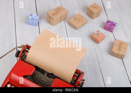 Holidays concept - red typewriter with blank craft paper, gift boxes on white wooden background Stock Photo