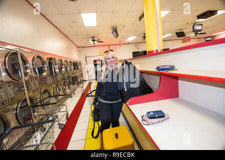 SAN DIEGO, CALIFORNIA: A blonde female does her laundry in a San Diego laundromat, holding her black laundry bag. Stock Photo
