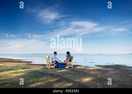 Two happy siblings playing a game with chess near the lake in nature Stock Photo