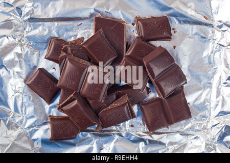 Several pieces of chocolate of the variety bittersweet lie on a silver paper. Stock Photo