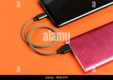 the smartphone is charging from a pink power bank on a yellow background Stock Photo