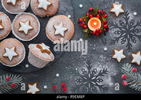 Top view of the wooden board  with sugar-sprinkled muffins, fondant icing and Christmas star cookies on dark background with candle Stock Photo