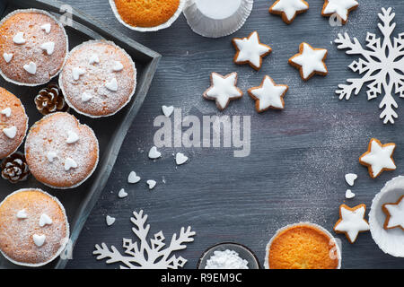 Top view of the table with sugar-sprinkled muffins, fondant icing and Christmas star cookies on dark wooden board Stock Photo