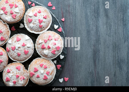 Sugar-sprinkled muffins with pink and white fondant icing hearts. Top view, birthday or Valentine concept. Stock Photo