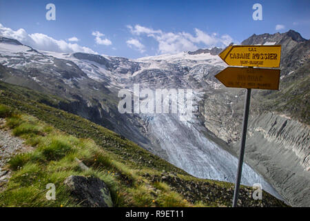 mountain landscape with green fields and snowy peaks and wild glacier in the Swiss Alps and yellow hiking trail signpost in the Zinal Valley in the Va Stock Photo