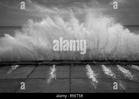 Scarborough seafront: Dramatic wave crashing against the sea wall in black and white Stock Photo