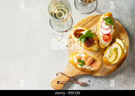 Italian Antipasti snacks set for Wine. Brushetta with Soft Cheese, Pear, Radish, Salmon and Dried Tomatoes on a light stone background. Top view flat  Stock Photo