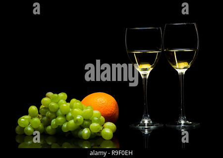 Three glasses for wine, a bunch of grapes and oranges on a black background, studio light Stock Photo