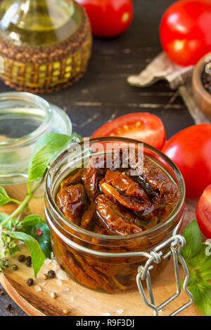 Sun dried tomatoes with olive oil in a jar on black stone or concrete table. Stock Photo