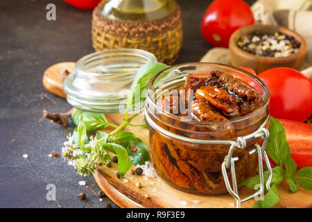 Sun dried tomatoes with olive oil in a jar on black stone or concrete table. Copy space. Stock Photo