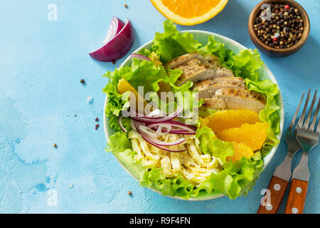 Diet menu. Healthy salad close-up, salad with chicken, egg pancakes, orange, green salad and dressing vinaigrette on a blue stone table. Copy space. Stock Photo