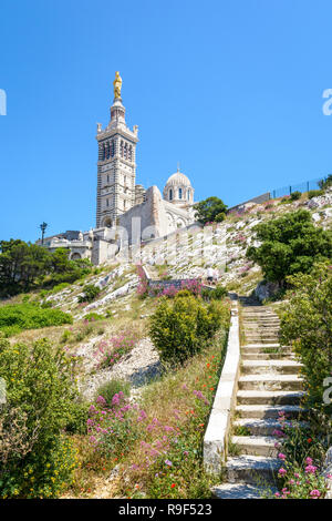 Low angle view of Notre-Dame de la Garde basilica on top of the hill in Marseille, France, seen from a secondary access trail with stairs in the rocks Stock Photo