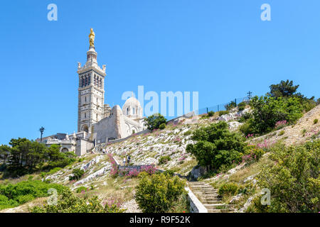 Low angle view of Notre-Dame de la Garde basilica on top of the hill in Marseille, France, seen from a secondary access trail with stairs in the rocks Stock Photo