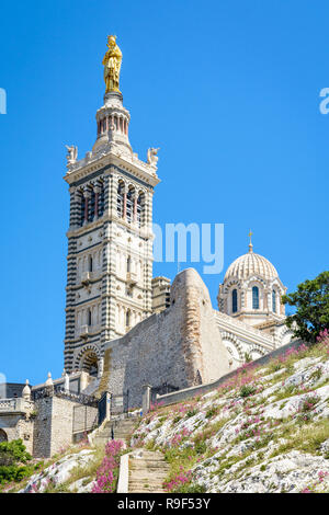 Low angle view of Notre-Dame de la Garde basilica on top of the hill in Marseille, France, seen from a secondary access trail with stairs in the rocks Stock Photo