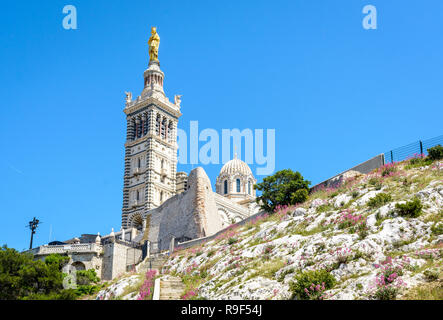 Low angle view of Notre-Dame de la Garde basilica on top of the hill in Marseille, France, seen from a secondary access trail with stairs in the rocks Stock Photo