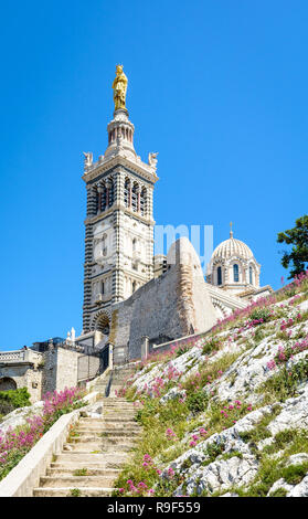 Low angle view of Notre-Dame de la Garde basilica on top of the hill in Marseille, France, seen from a secondary access trail with stairs in the rocks Stock Photo