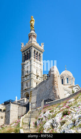 Low angle view of Notre-Dame de la Garde basilica on top of the hill in Marseille, France, seen from a secondary access trail with stairs in the rocks Stock Photo