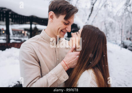 young guy and beautiful girl kiss in a snowy park. Couple in sweaters. Stock Photo