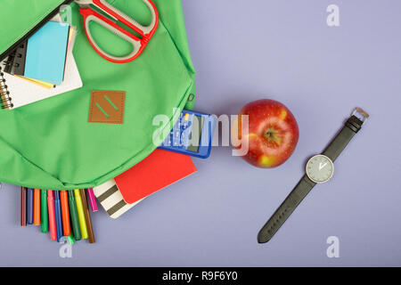 Backpack and school supplies: notepad, felt-tip pens, scissors, calculator, watch on blue paper background Stock Photo