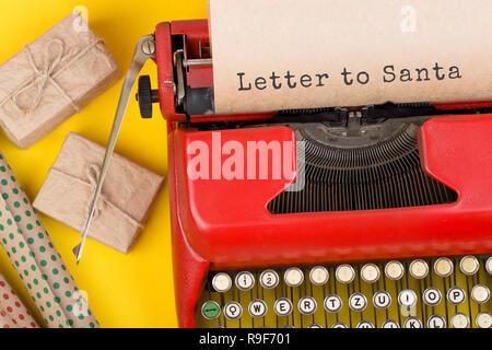 Christmas concept - red typewriter with the text "Letter to Santa," gift boxes and wrapping paper on yellow background Stock Photo