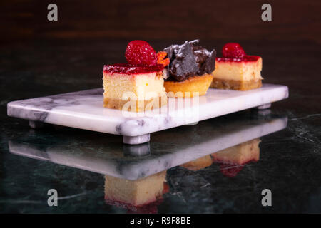 Set of mini cakes in assortment on white plate. Restaurant menu. Blackberry cake with raspberries. Tartlet with fruits. Close up. Stock Photo