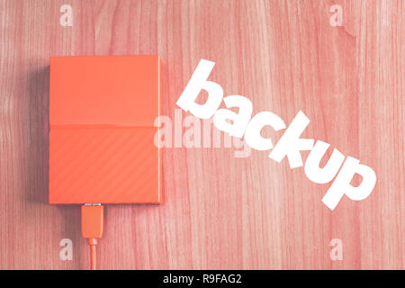 Portable external hard drive on the desk next to inscription 'BACKUP'. Stock Photo