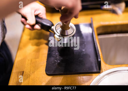 Man is using a tamper to press freshly ground morning coffee into a coffee tablet Stock Photo
