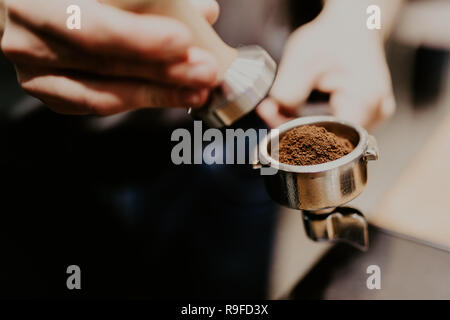 Man is using a tamper to press freshly ground morning coffee into a coffee tablet Stock Photo