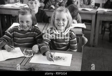 1950s, historical, primary school children, Langbourne School, England, UK. Picture shows two smiling young girls- possibly twin sisters as they look alike and are wearing identical jumpers - sitting next to each other at a wooden two-seater  desk doing an art class. Stock Photo