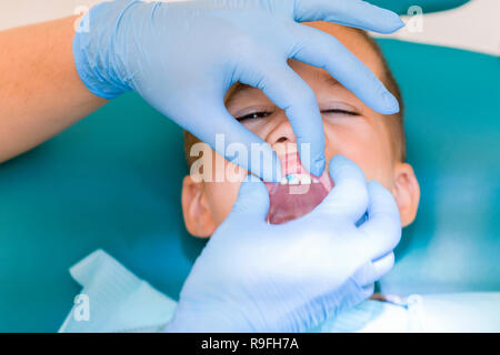 Pediatric dentist examining a little boys teeth in the dentists chair at the dental clinic. Dentist examining little boy's teeth in clinic. Stock Photo